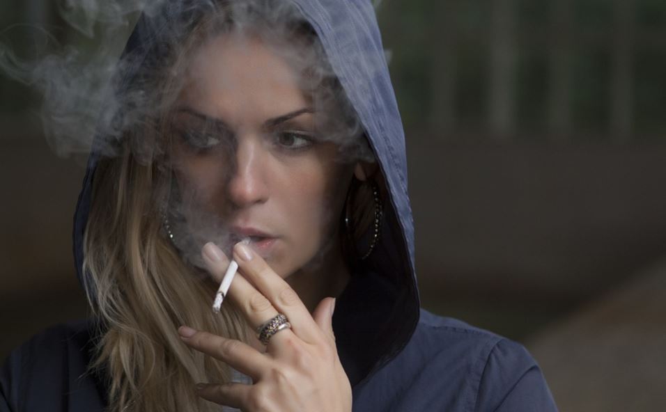Chica joven fuma con la capucha puesta.