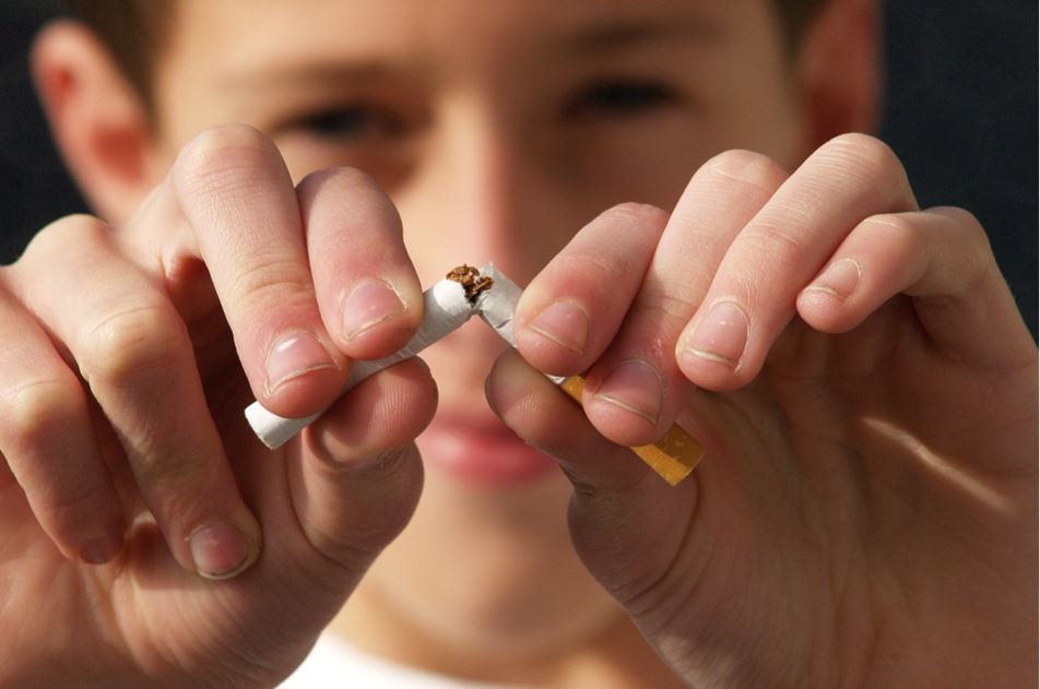 Un chico rompiendo un cigarro por la mitad como gesto de no fumar.