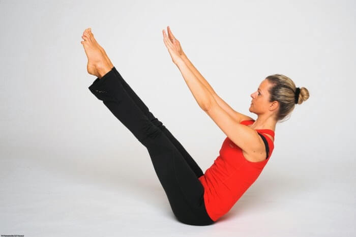 Para hacer la V, levanta tus piernas y flexiona las rodillas para que queden en posición horizontal y levanta la espalda haciendo que los brazos pasen sobre las rodillas.