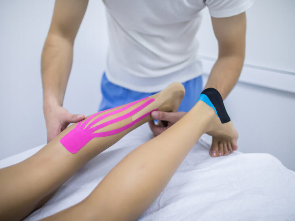 Fisioterapeuta aplica taping en la pierna a paciente.