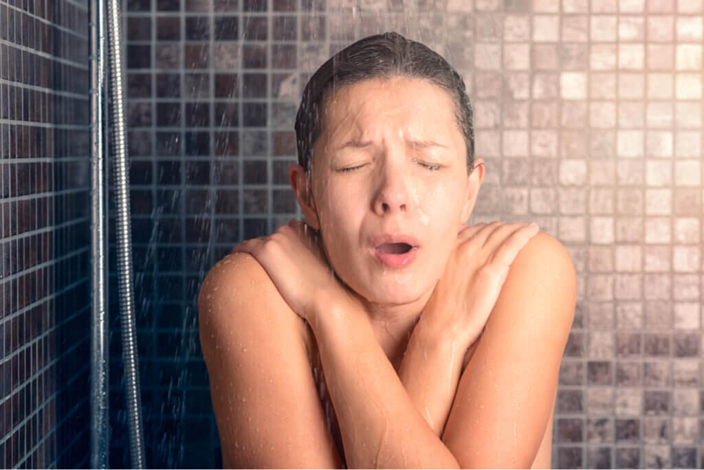 Mujer se ducha con agua fría para mejorar la recuperación muscular.