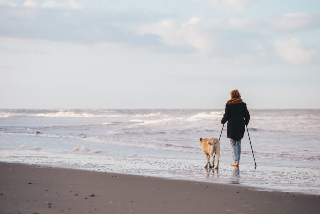 Mujer realizando caminata nórdica en la playa con su perro.