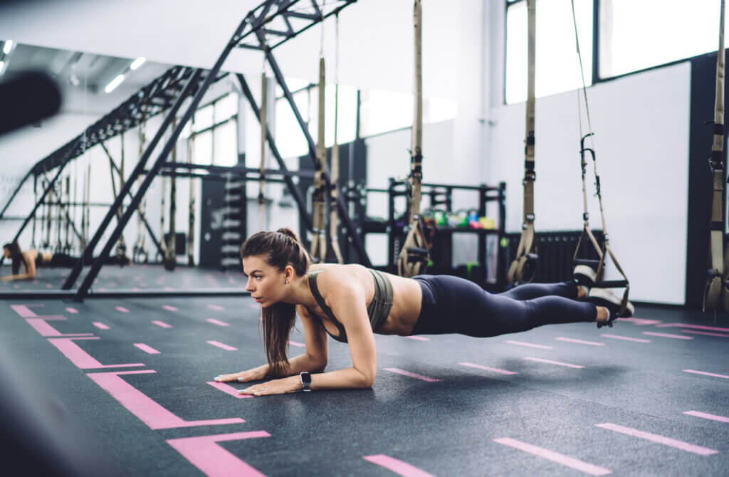 Woman doing forearm plank as part of a beginner TRX routine.