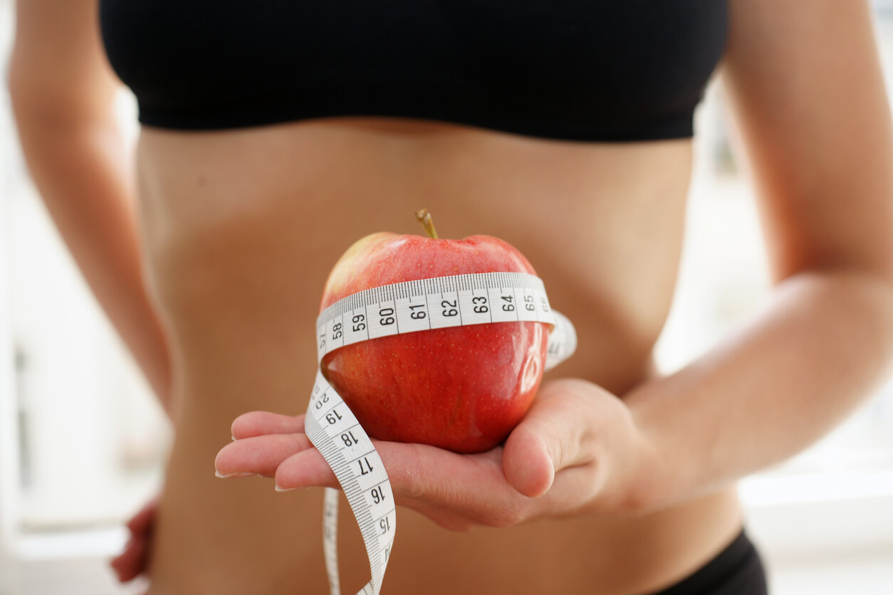 Mujer sosteniendo manzana y cinta métrica tras aplicar consejos para mantener la dieta