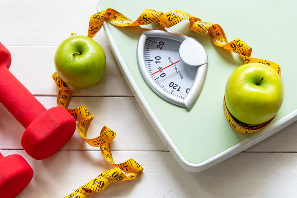 Balanza, cinta métrica y manzana que forman parte de las calorías buenas