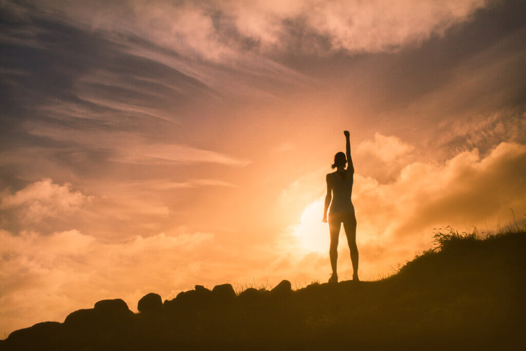 Mujer sobre la cima de un monte elevando su puño en señal de satisfacción