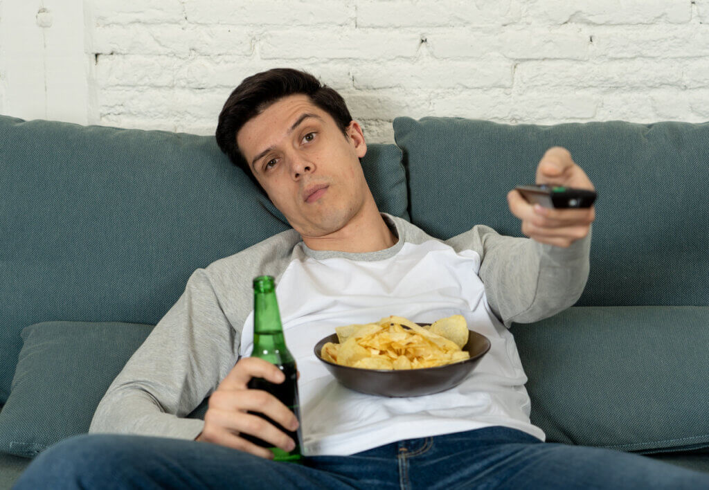 Hombre sedentario comiendo papas fritas y bebiendo cerveza