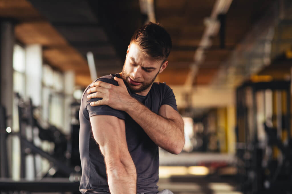 Hombre sujetando su hombro tras sufrior una lesión frecuente en el gimnasio