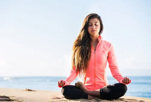 Mujer haciendo yoga en la playa para relajarse