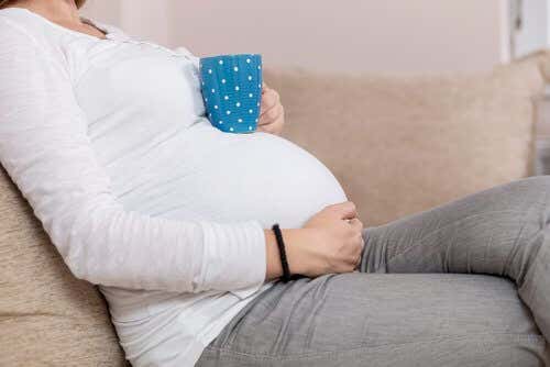 Mujer embarazada sentada con taza sobre barriga 