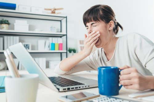 Mujer bostezando con una taza ante el ordenador.