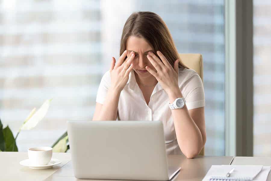 Mujer estresada frente al ordenador haciéndose un masaje en los ojos.