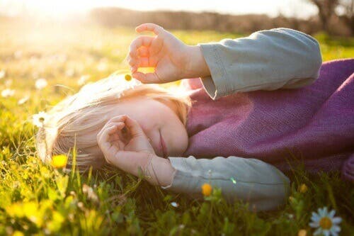 Niña tumbada en el césped con una flor en la mano pensando en los noviazgos entre los niños.