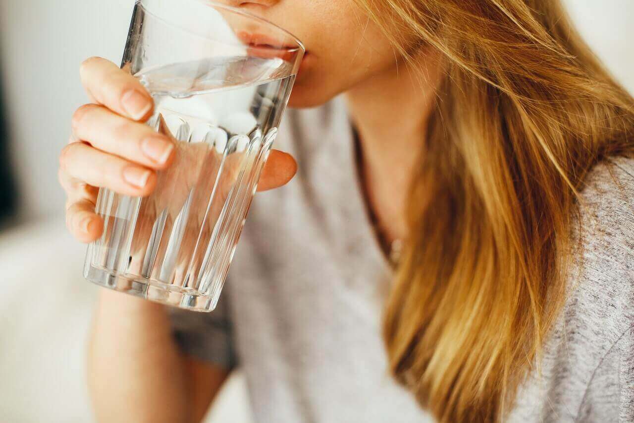 Mujer bebiendo un vaso de agua fría.