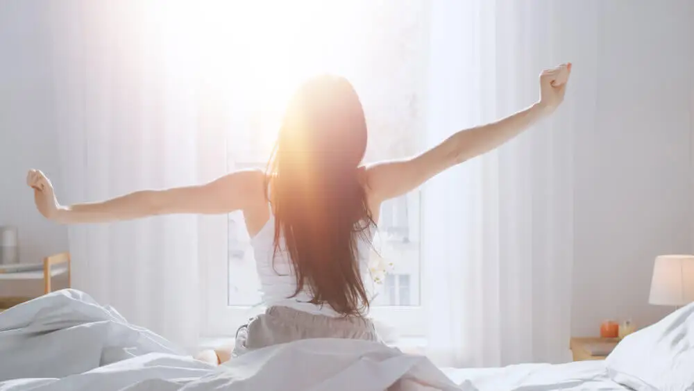 Mujer estirándose en la cama con ánimo