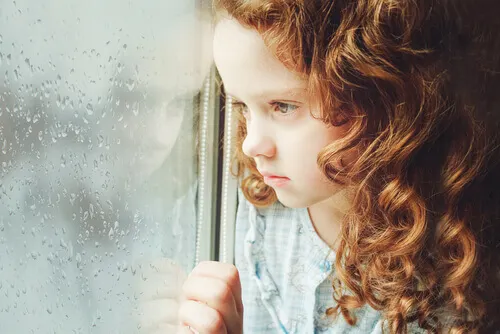 Niña triste mirando por la ventana.