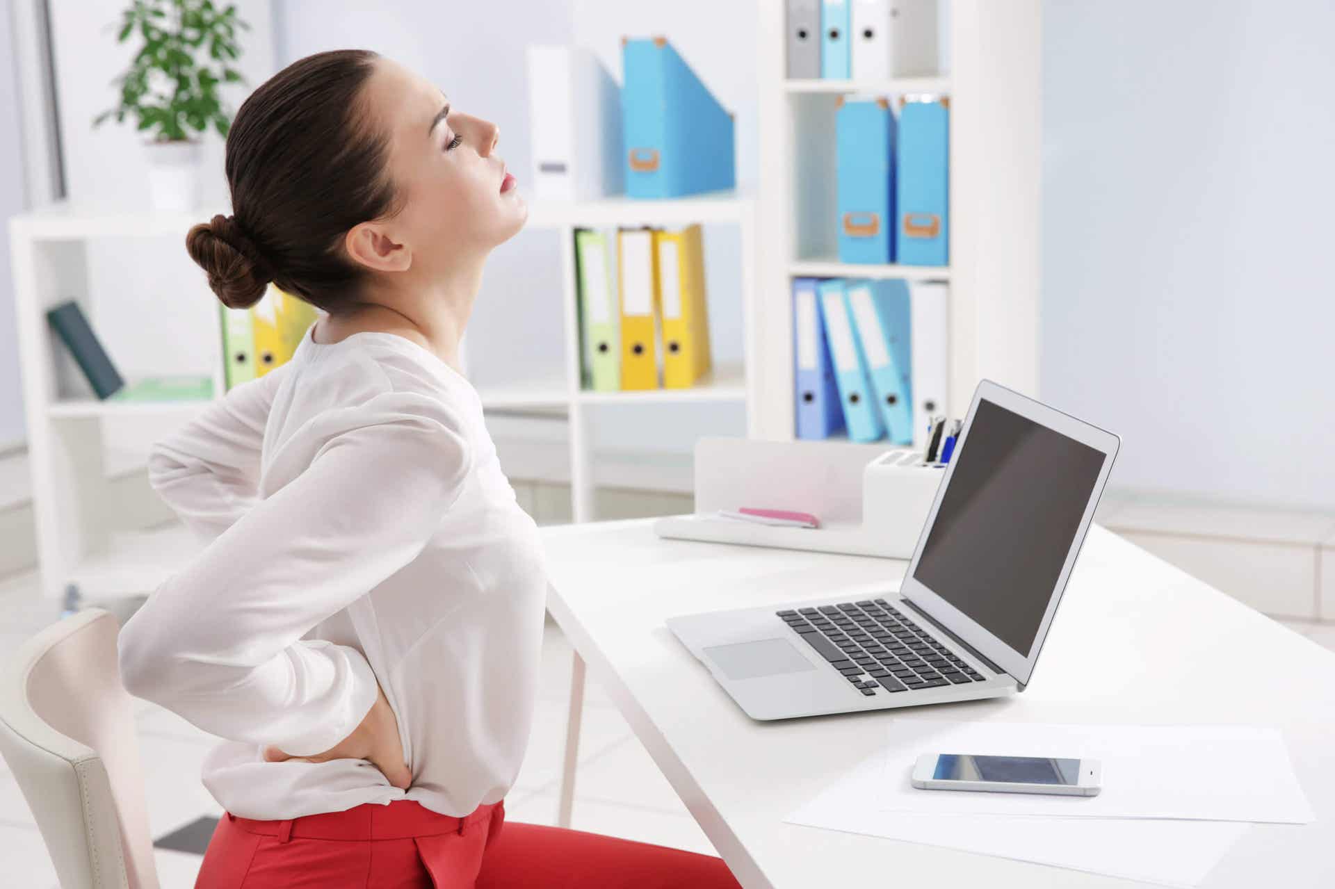 Kyphose - Frau mit Rückenschmerzen an einem Schreibtisch