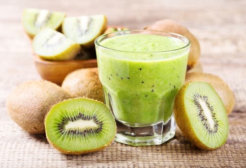 Licuado de kiwi rodeado de kiwis cortados