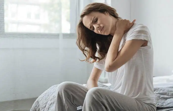 Mujer levantándose de la cama con torticolis