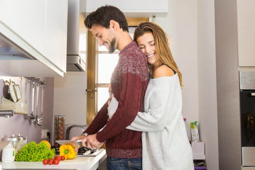 Chica abrazando a su pareja en la cocina.
