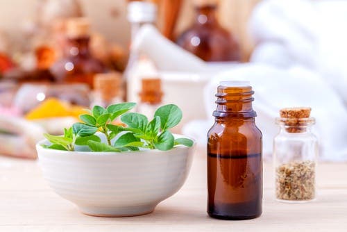 Aceite de orégano junto a un bol con hojas de la planta