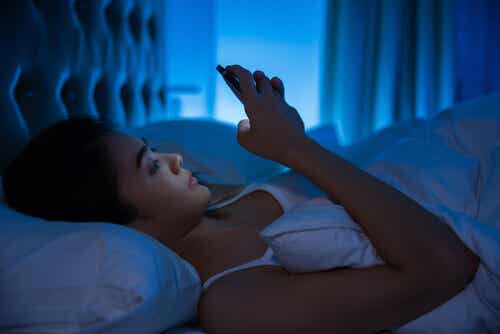 Mujer en la cama con el teléfono móvil.