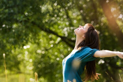 Mujer feliz abriendo los brazos bajo el sol.