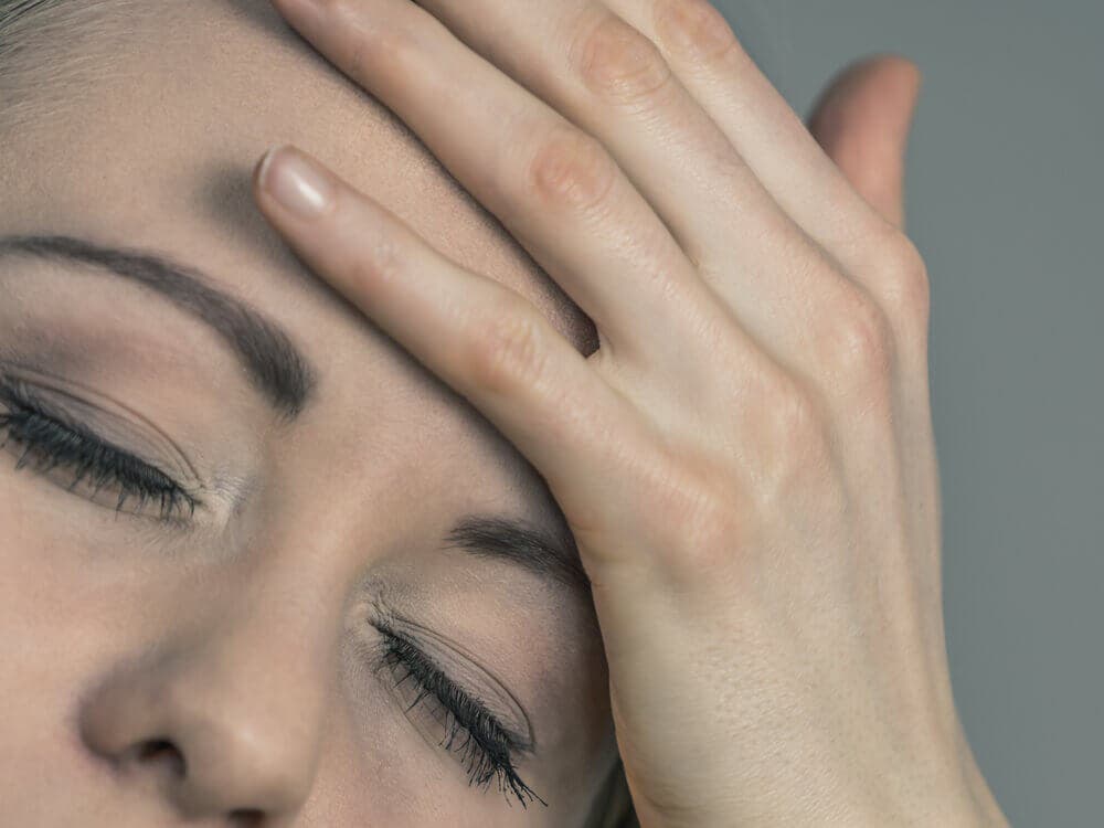 mujer con la mano en el rostro por dolor de cabeza.