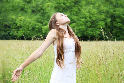 Mujer joven llenando sus pulmones de aire en una pradera.