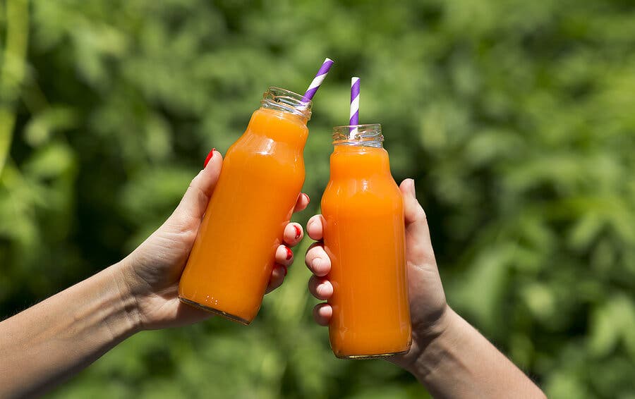 Manos sosteniendo botellas de zumo de zanahoria.