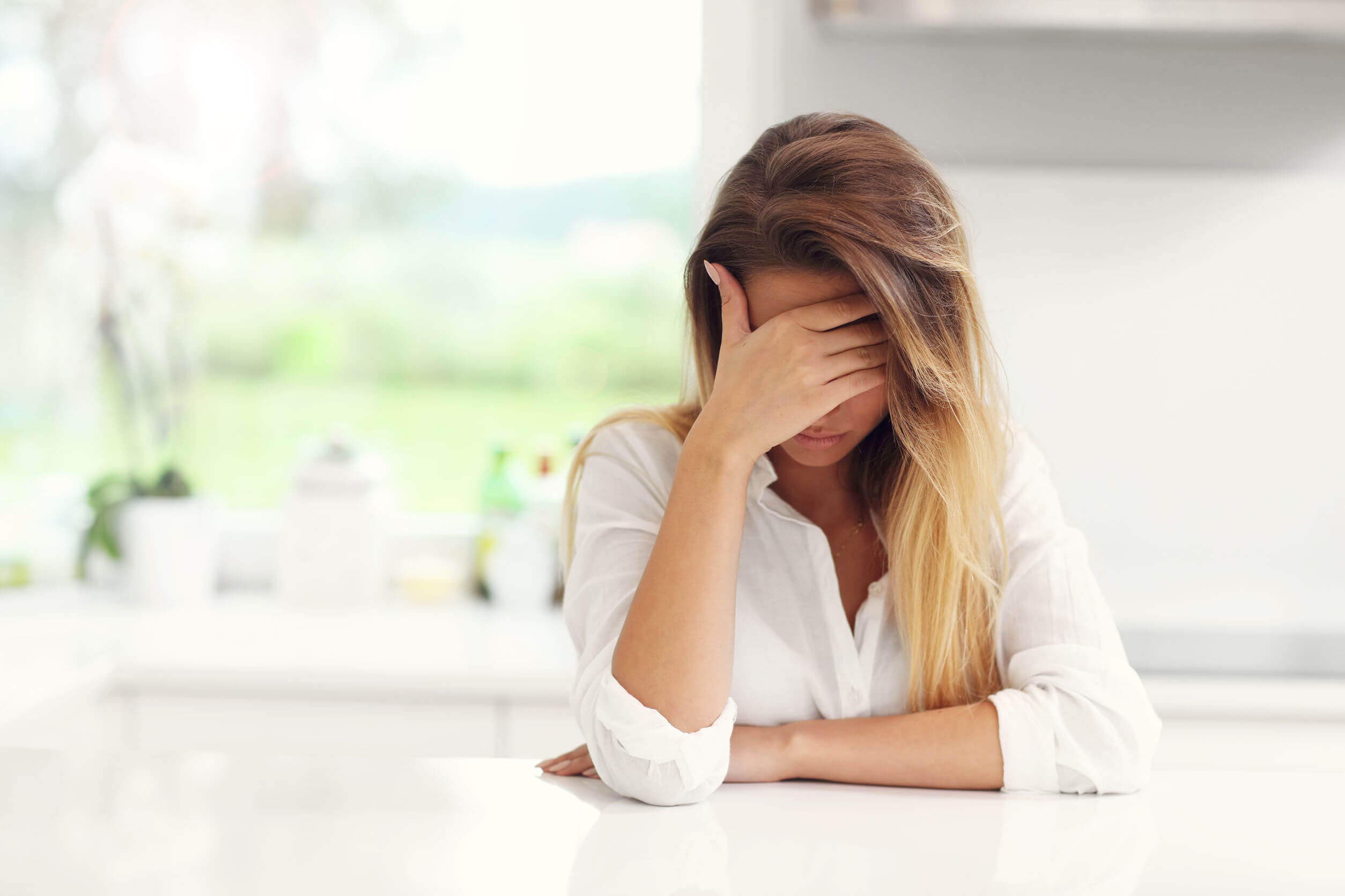 Mujer triste cubriéndose el rostro con una mano.