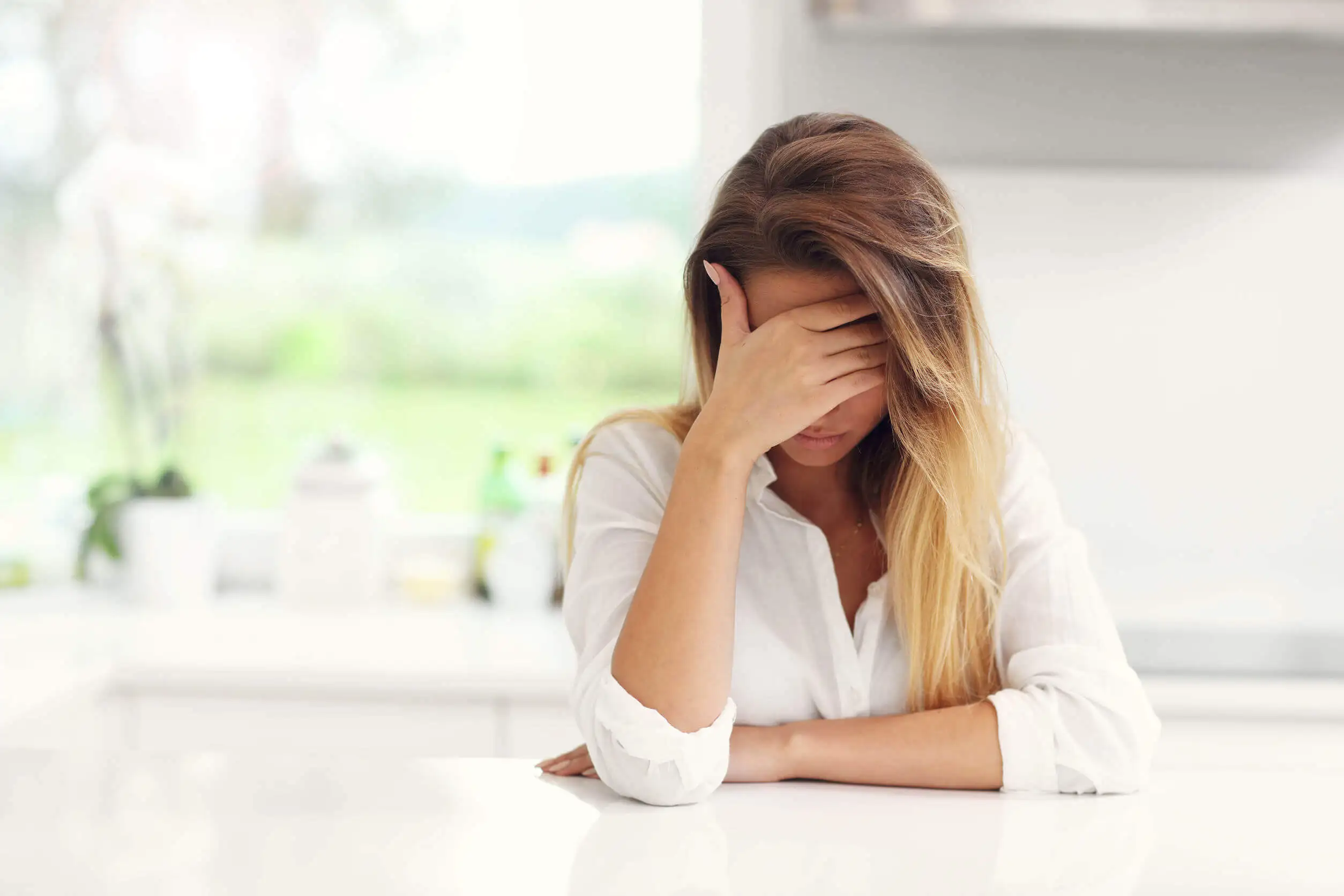 Mujer triste cubriéndose el rostro con una mano.