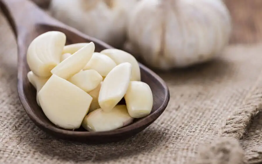 Cuchara de madera con dientes de ajo pelados.