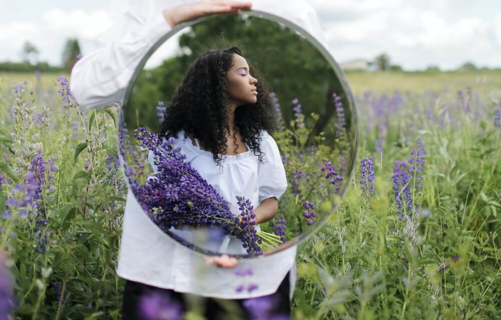 Mujer sujetando un espejo en un campo de lavanda.