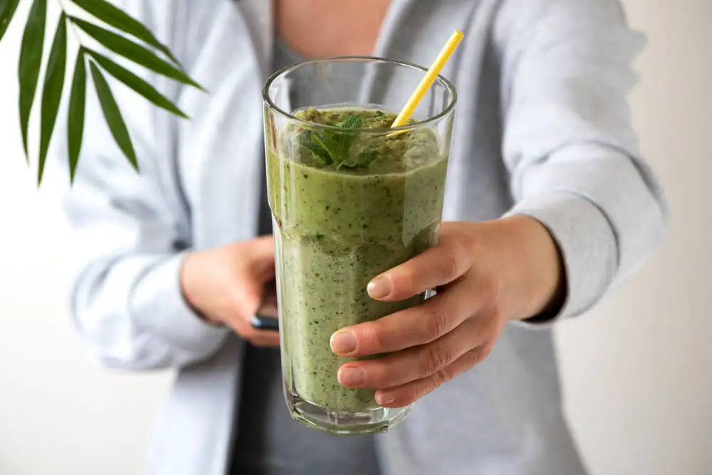 Mujer sostiene vaso de batido verde