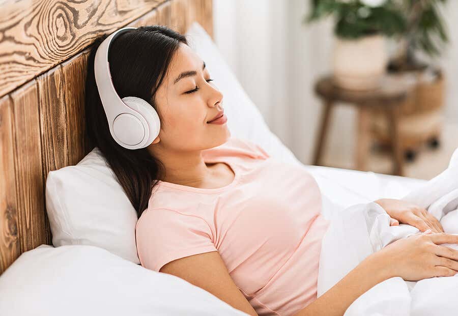 Mujer con cascos escuchando música relajante en su cama.