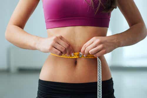 Mujer midiéndose con una cinta métrica el contorno del abdomen después de seguir una dieta cetogénica