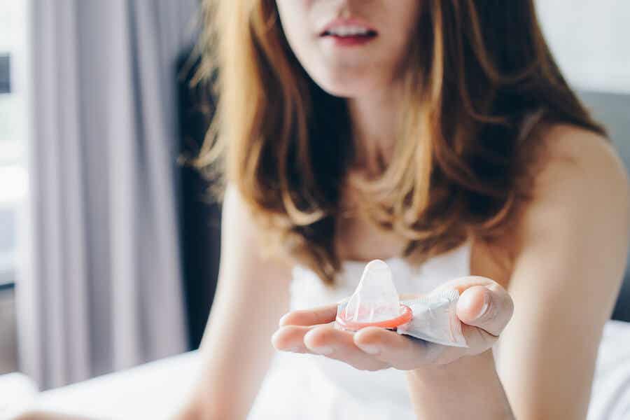 Mujer en la cama sosteniendo un preservativo en la mano.