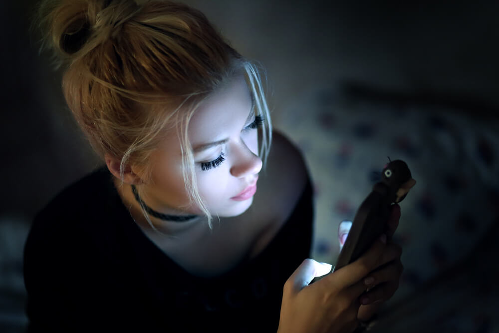 Mujer joven mirando su teléfono móvil a oscuras.