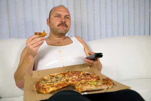 Señor en el sofá viendo la tele mientras se come una pizza