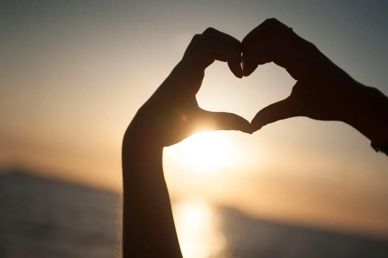 Manos formando un corazón al atardecer.