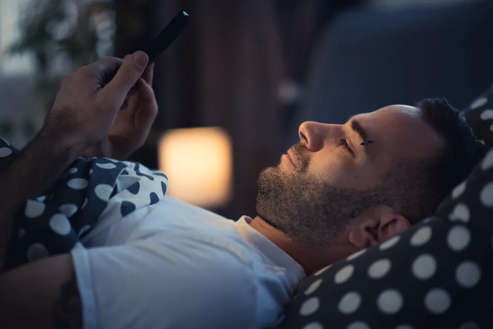 L'homme regarde le mobile au lit parce qu'il n'a pas sommeil.