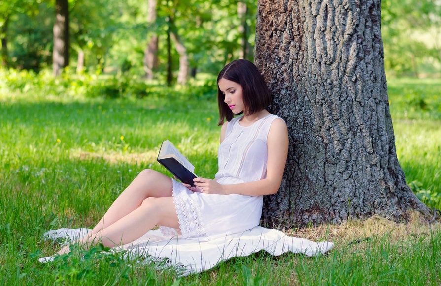 Femme lisant un livre sous un arbre.