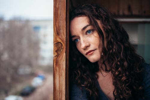 Mujer pensativa y triste mirando por la ventana,