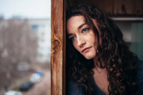 Mujer pensativa y triste mirando por la ventana,