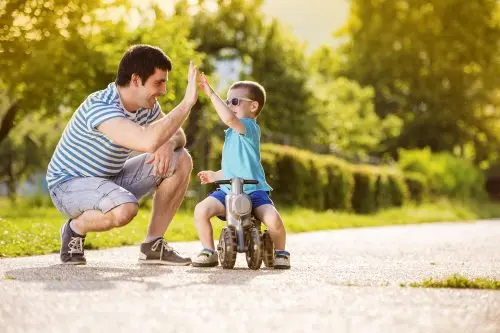 Padre chocando la mano con un niño en triciclo por el parque.