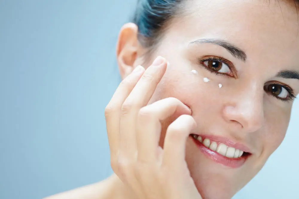 Mujer joven aplicándose crema en el contorno de los ojos.