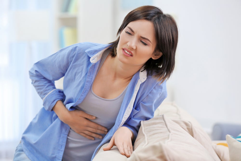 Mujer tocándose el abdomen con cara de dolor como consecuencia de la pancreatitis que sufre