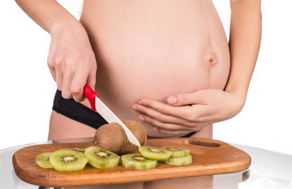 Mujer embarazada partiendo un kiwi.