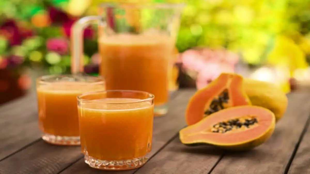 Dos vasos de jugo de papaya, con una jarra y dos mitades de esta fruta.